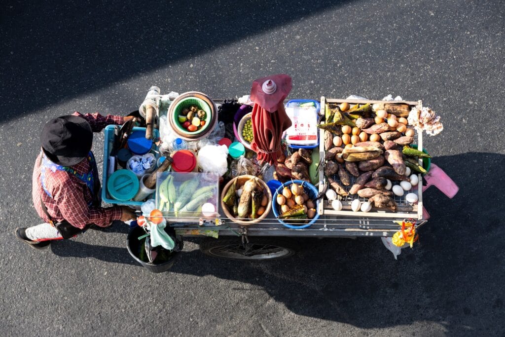 Overhead view looking down on a woman pushing a cart laden with vegetables in Bangkok