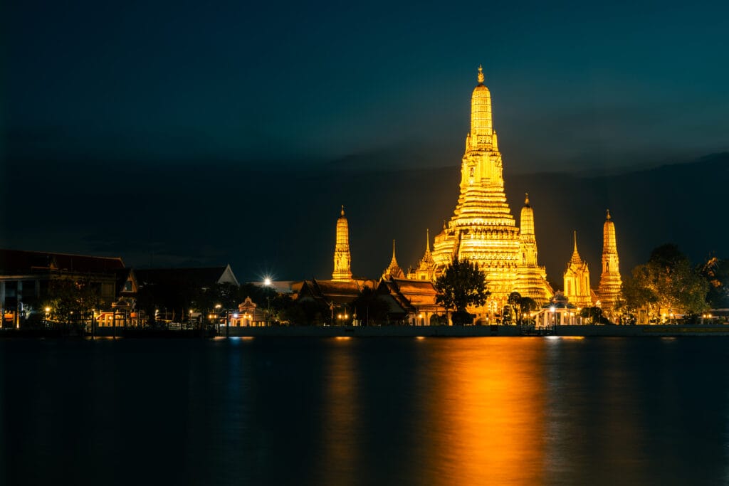 Wat Arun across the Chao Phraya river at night The golden light of the temple is reflected in the river. Long exposure makes the river
