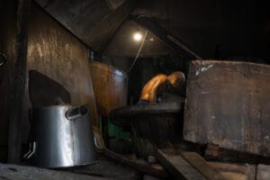 The dark interior of a soy factory in Bangkok illuminated by a single lightbulb with a man stooping over working