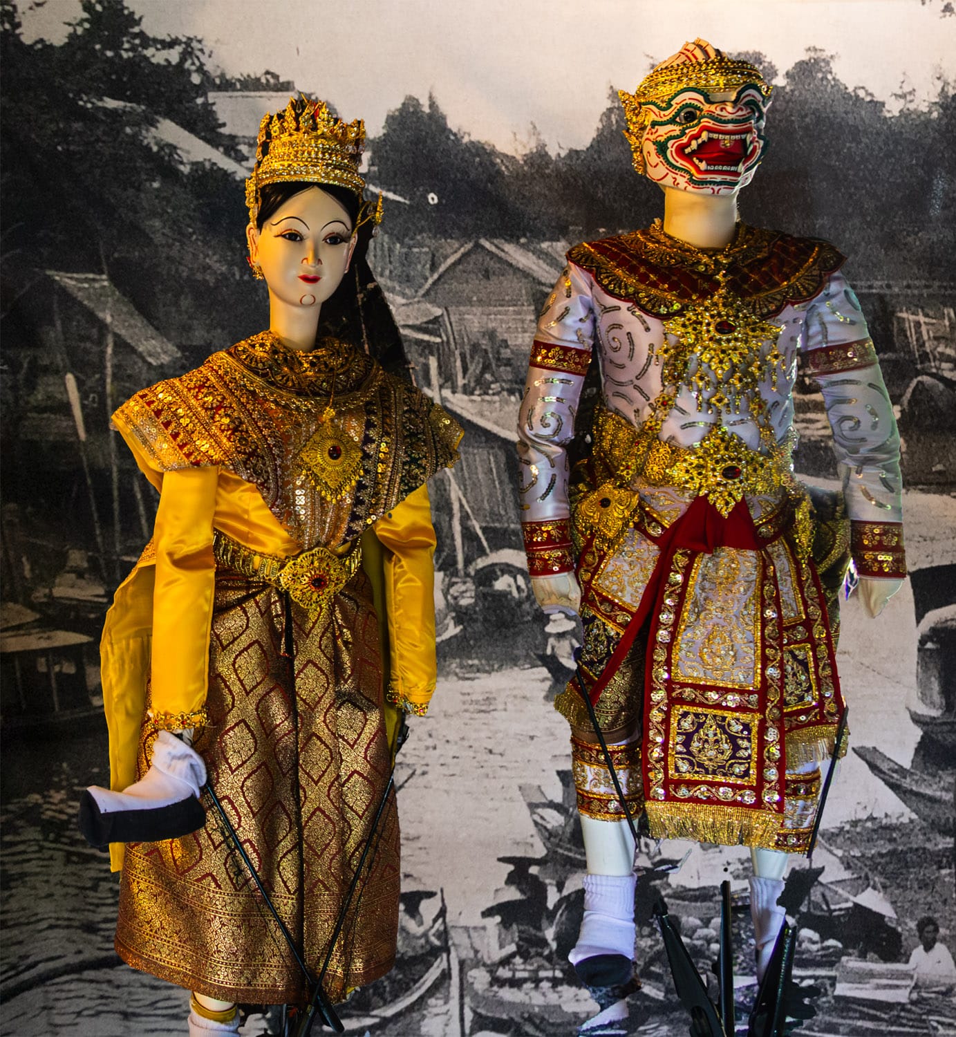 Ornate puppets used in the Artist House puppet show in front of an old black-and-white photograph of a Bangkok Canal