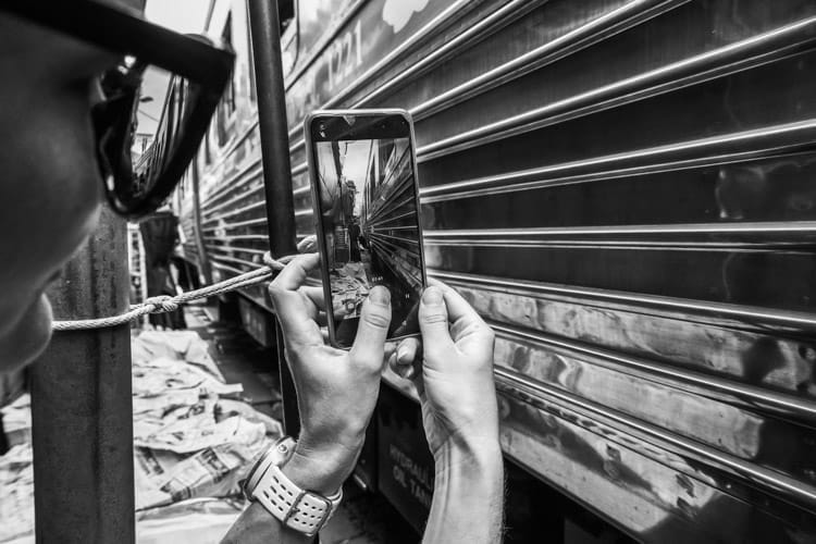 View of the mobile phone screen of a woman filming the Mae Klong Railway market train as it passes very close by
