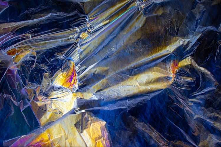 A stretched plastic bag reveals colourful stress patterns under polarised light