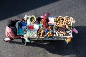 View from above looking down on a woman pushing a market cart laden with produce, in Bangkok